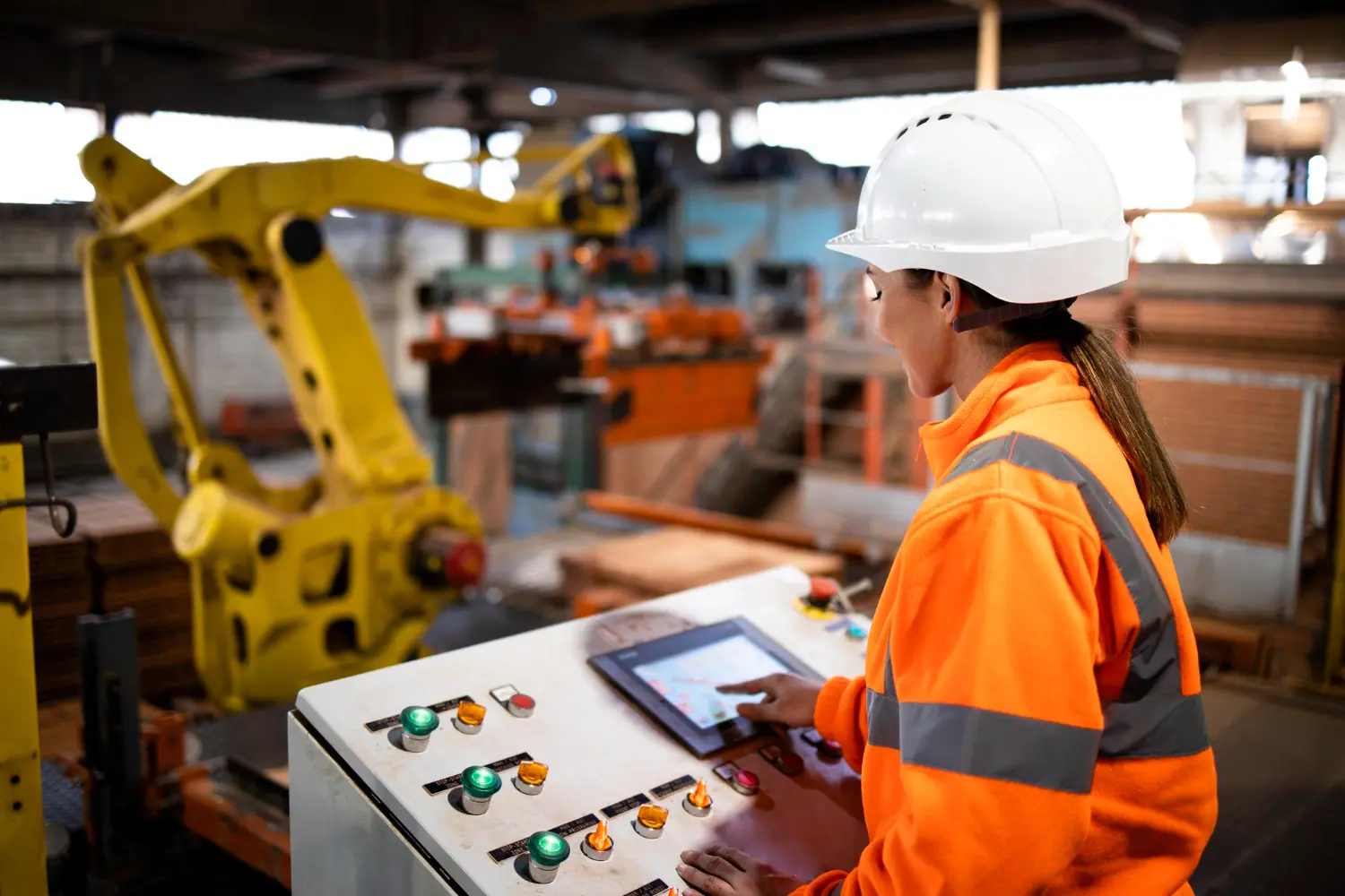 Operadora controla célula robotizada industrial por painel digital, aplicando os requisitos da NR 12 para segurança em máquinas e equipamentos automatizados.