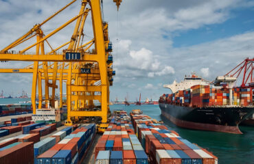 Carregamento ativo de contêineres com guindastes pórtico. A logística entre cais e embarcação garante produtividade e integridade da carga.