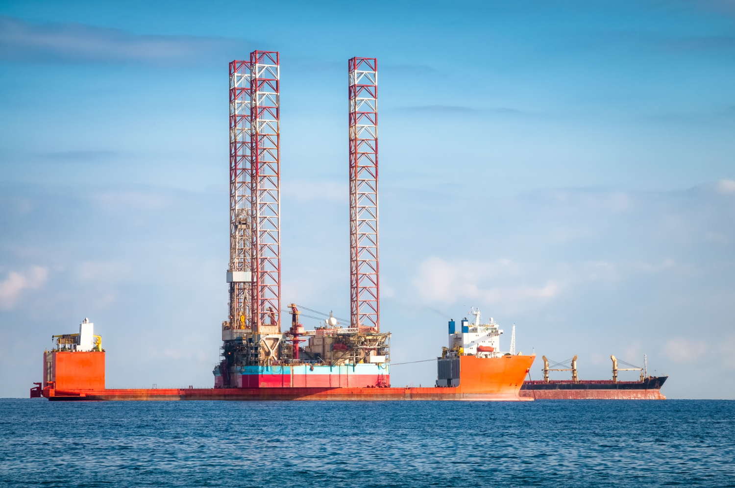 Unidade autoelevatória (Jack-Up) posicionada para operação de perfuração, com apoio logístico de embarcação de suprimentos no ambiente offshore. - Curso NR 37 - Nível Avançado.