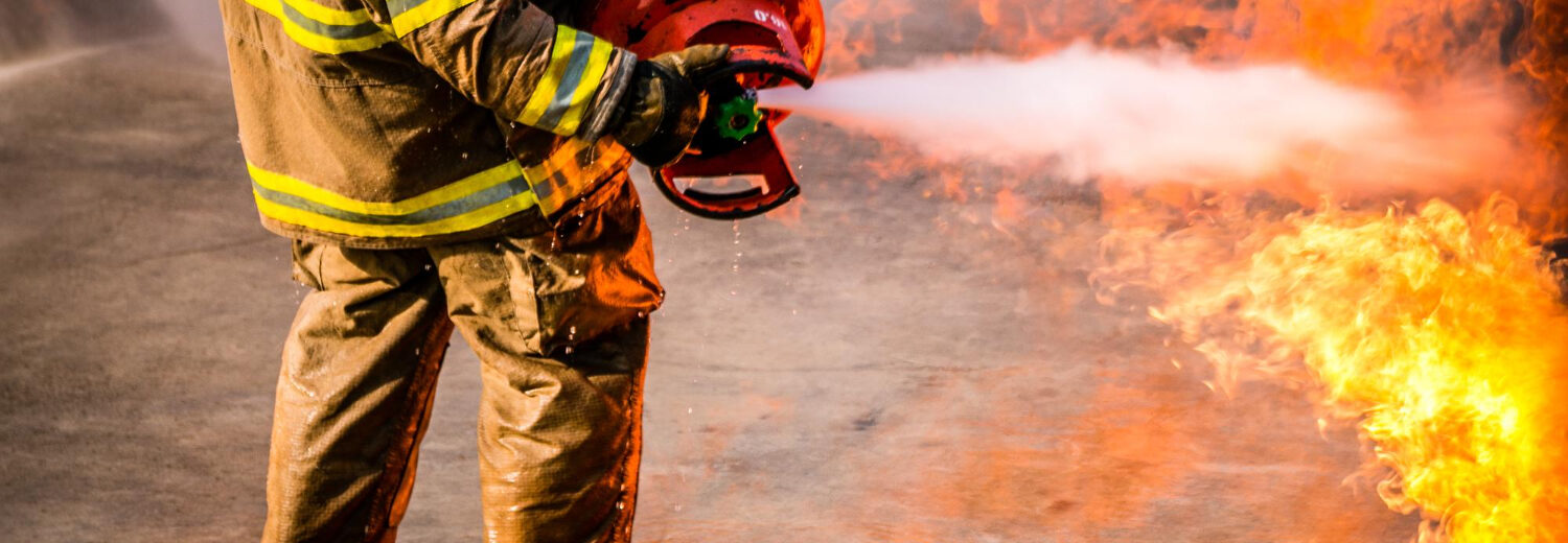 Seção baixa de bombeiro pulverizando extintor em chamas. - Consultoria NR 23