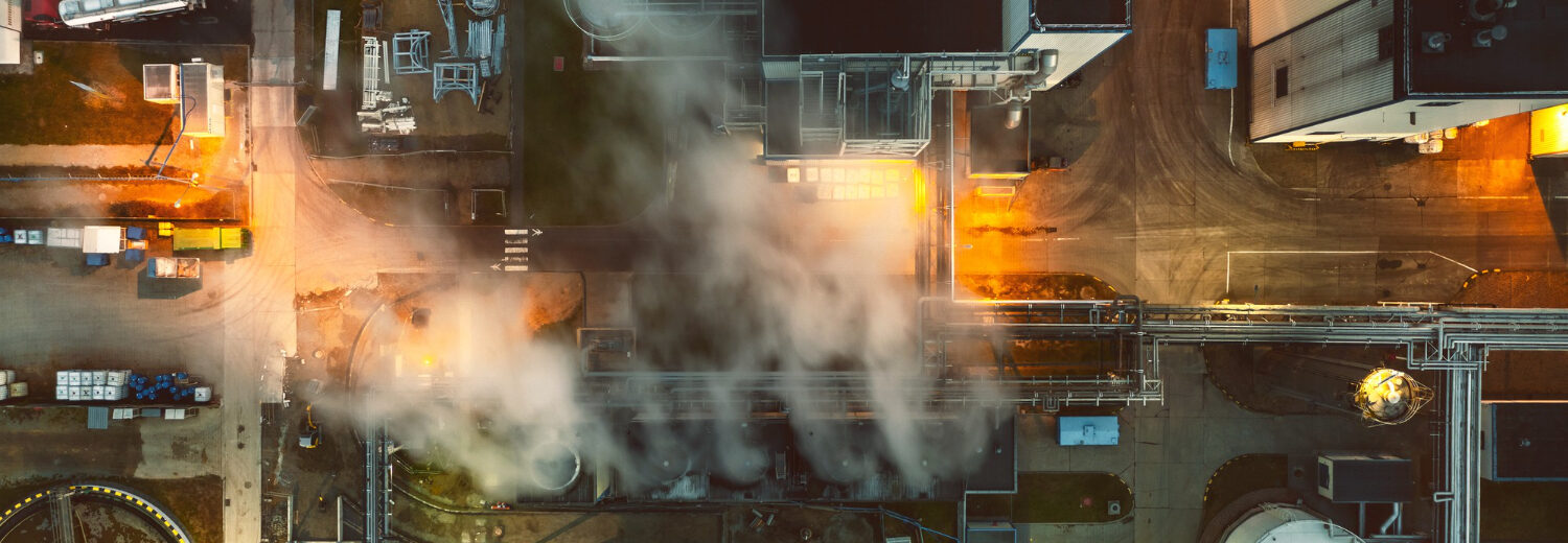 Vista aérea de uma instalação industrial fervilhante, com vapores escapando das tubulações e uma iluminação dramática, criando uma sensação de instabilidade em um ambiente potencialmente explosivo.