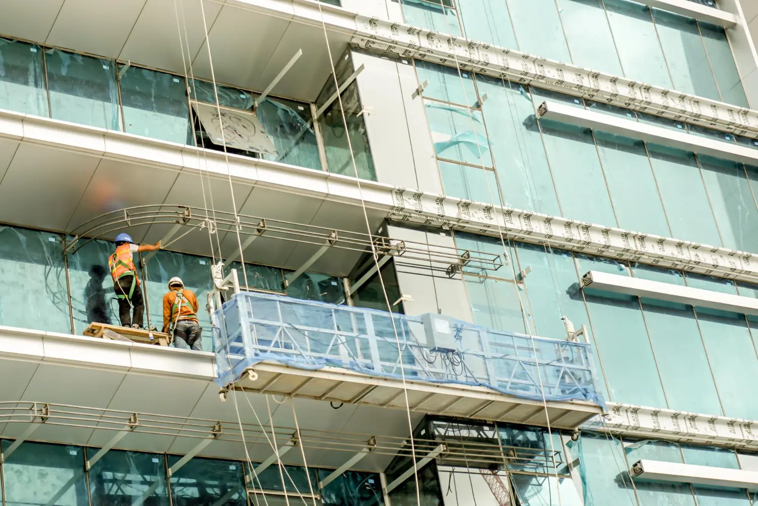 Montagem de fachada com plataforma suspensa em altura, trabalho controlado por ancoragem técnica e plano de gerenciamento de riscos.