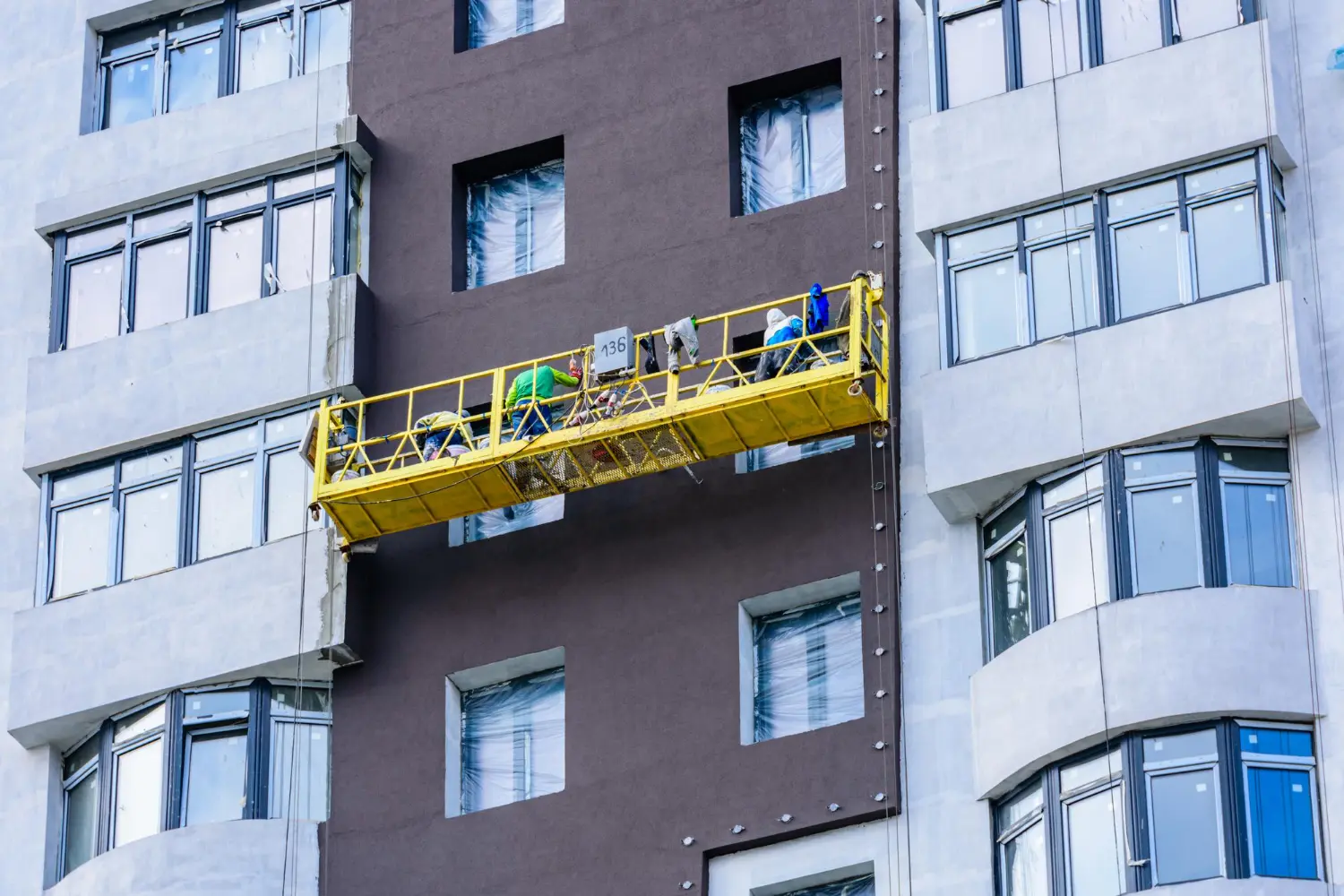 Trabalhadores utilizando plataforma suspensa na fachada de edifício, operação exige capacitação conforme NR 18, NR 35 e uso obrigatório de EPIs.