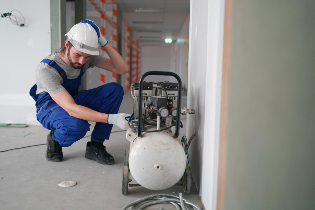 Worker inspecting a portable air compressor to verify structural integrity and pressure safety before activation.