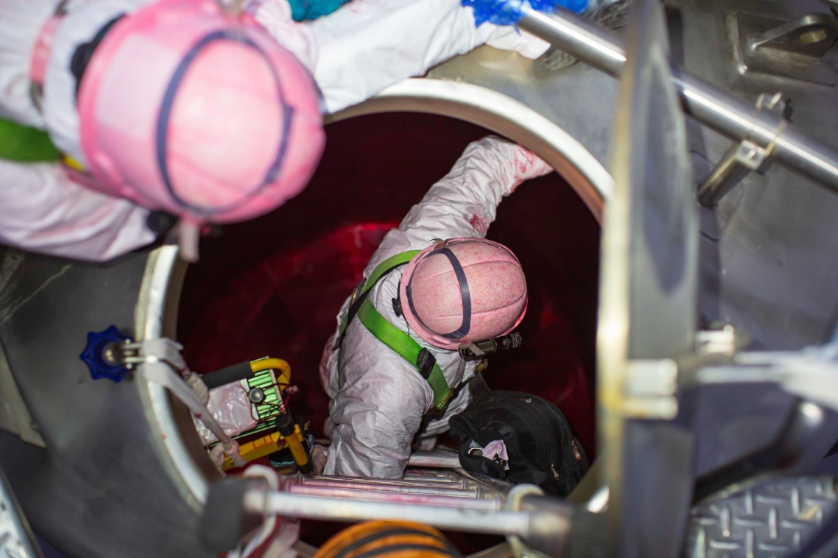 Rescue team entering a confined vessel with full PPE, direct-reading instruments and controlled descent for emergency operations.
