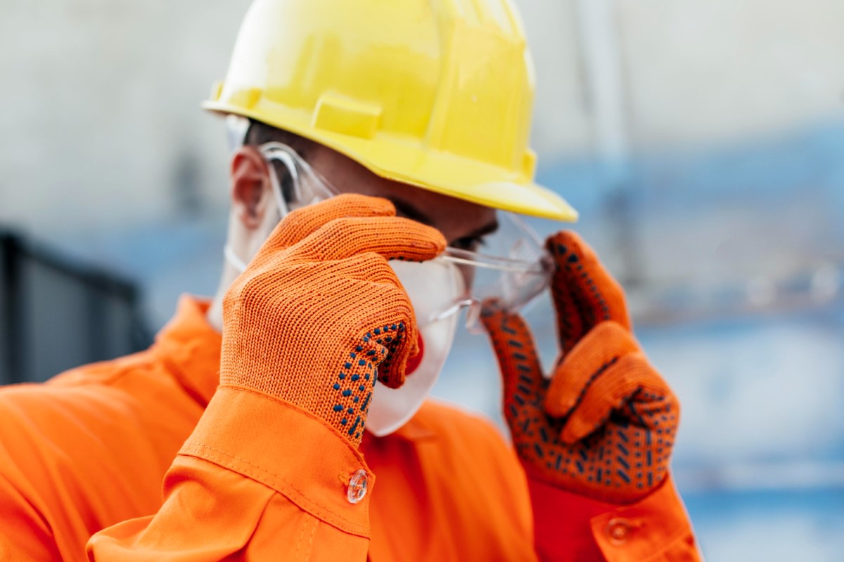 Worker adjusting eye protection to ensure correct fit and compliance with hazard control requirements during field activities.