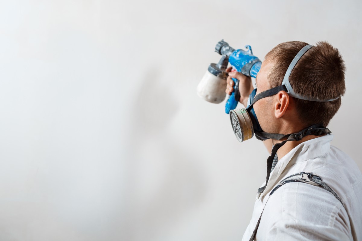 Worker using respiratory protection and spray equipment to maintain safety and stability during material application.
