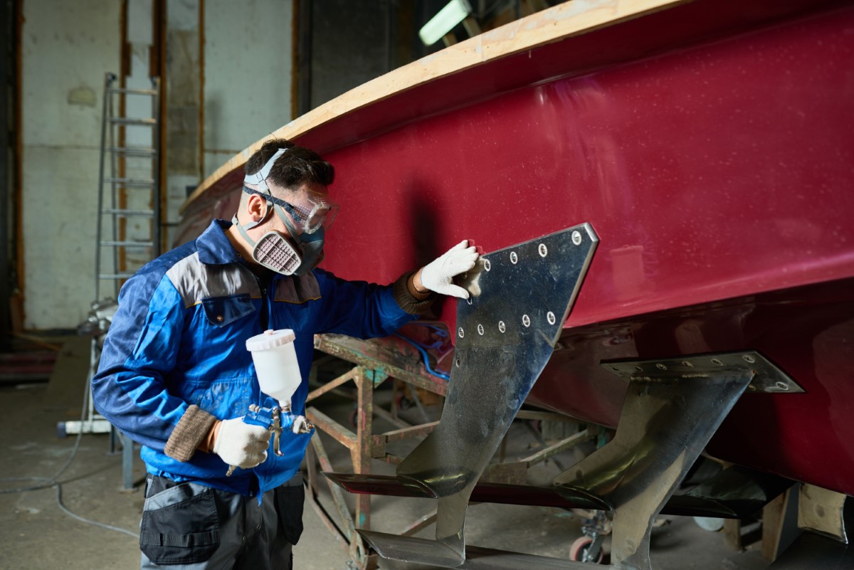 Surface preparation and spray painting on a vessel component, reinforcing the importance of respiratory protection, controlled ventilation and chemical hazard management under NR 34.