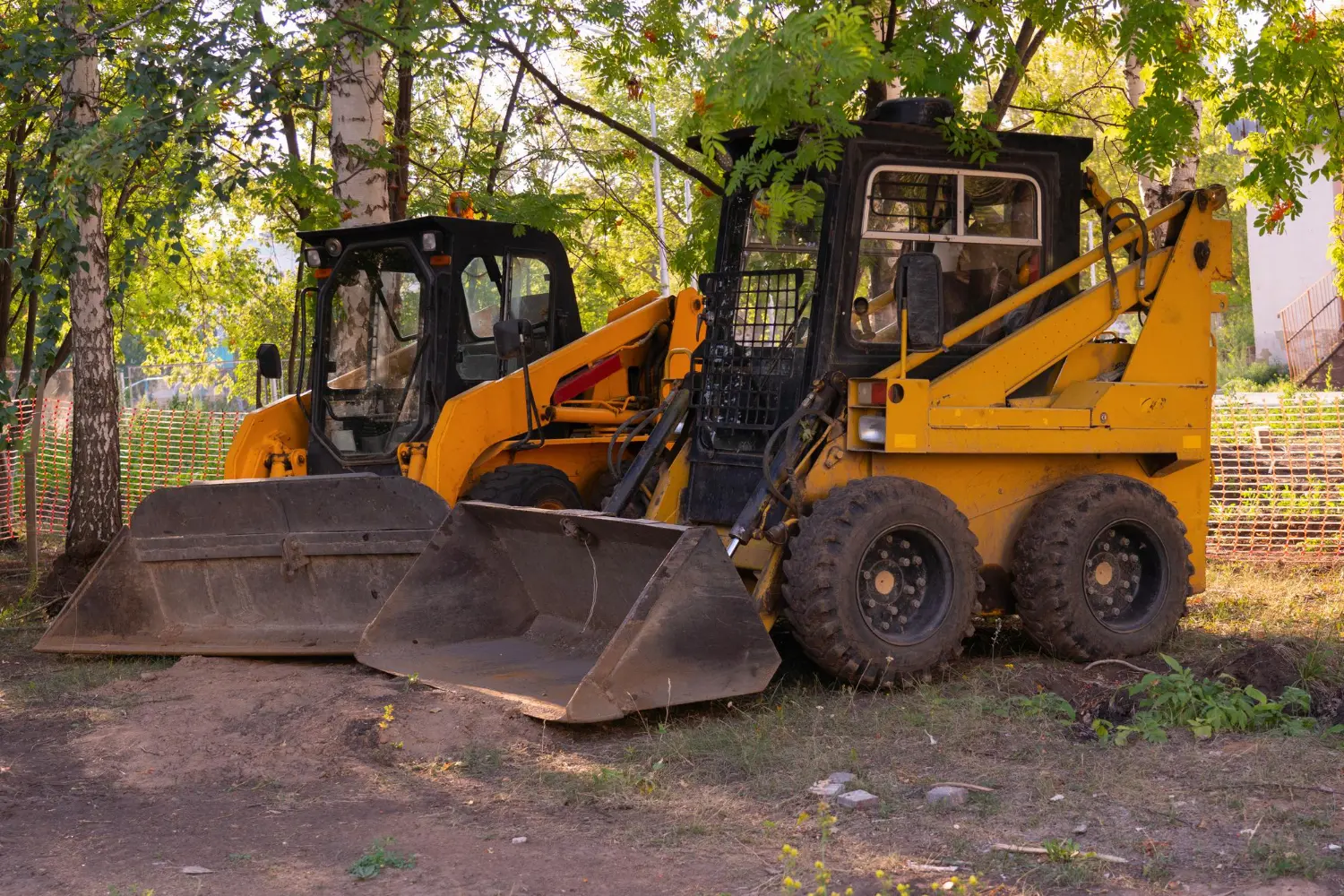 Duas mini carregadeiras paradas em área arborizada, prontas para manutenção e checklist diário obrigatório.