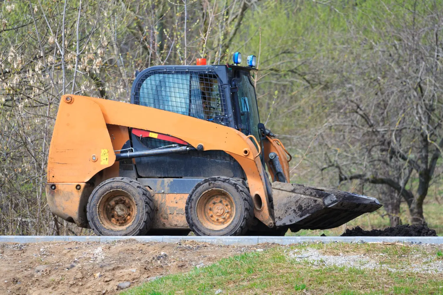 Mini carregadeira Bobcat em operação com caçamba rebaixada, demonstrando equilíbrio e preparo para deslocamento com material