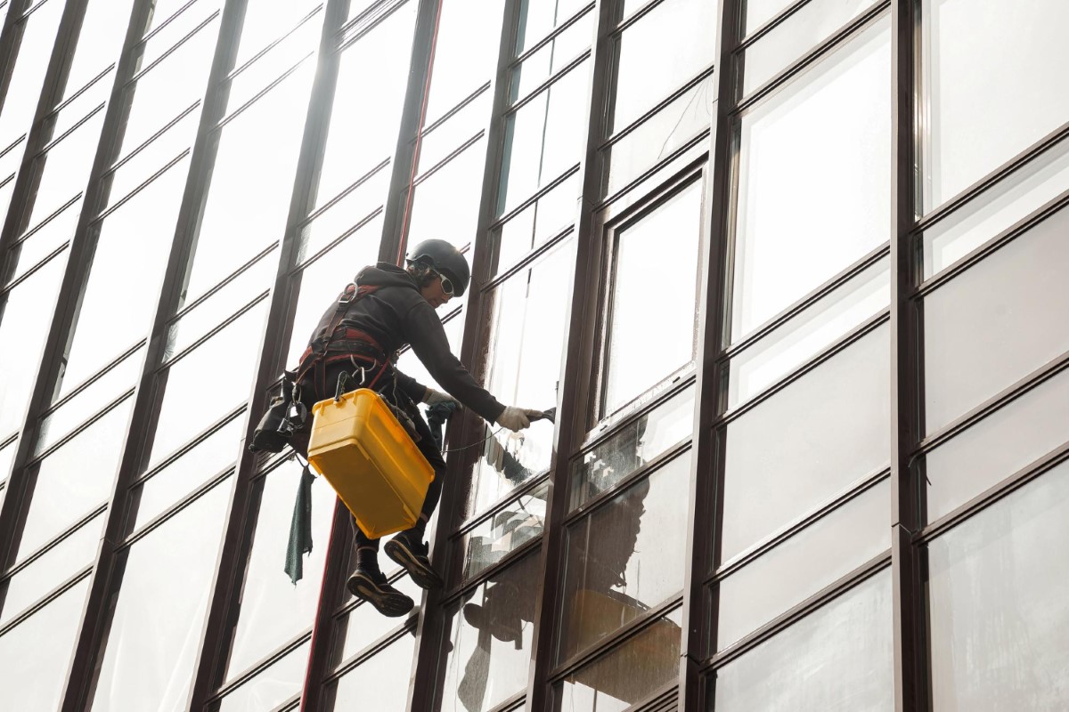Suspended access technician executes window cleaning using a manual bosun chair, applying safe load distribution and continuous rope management.