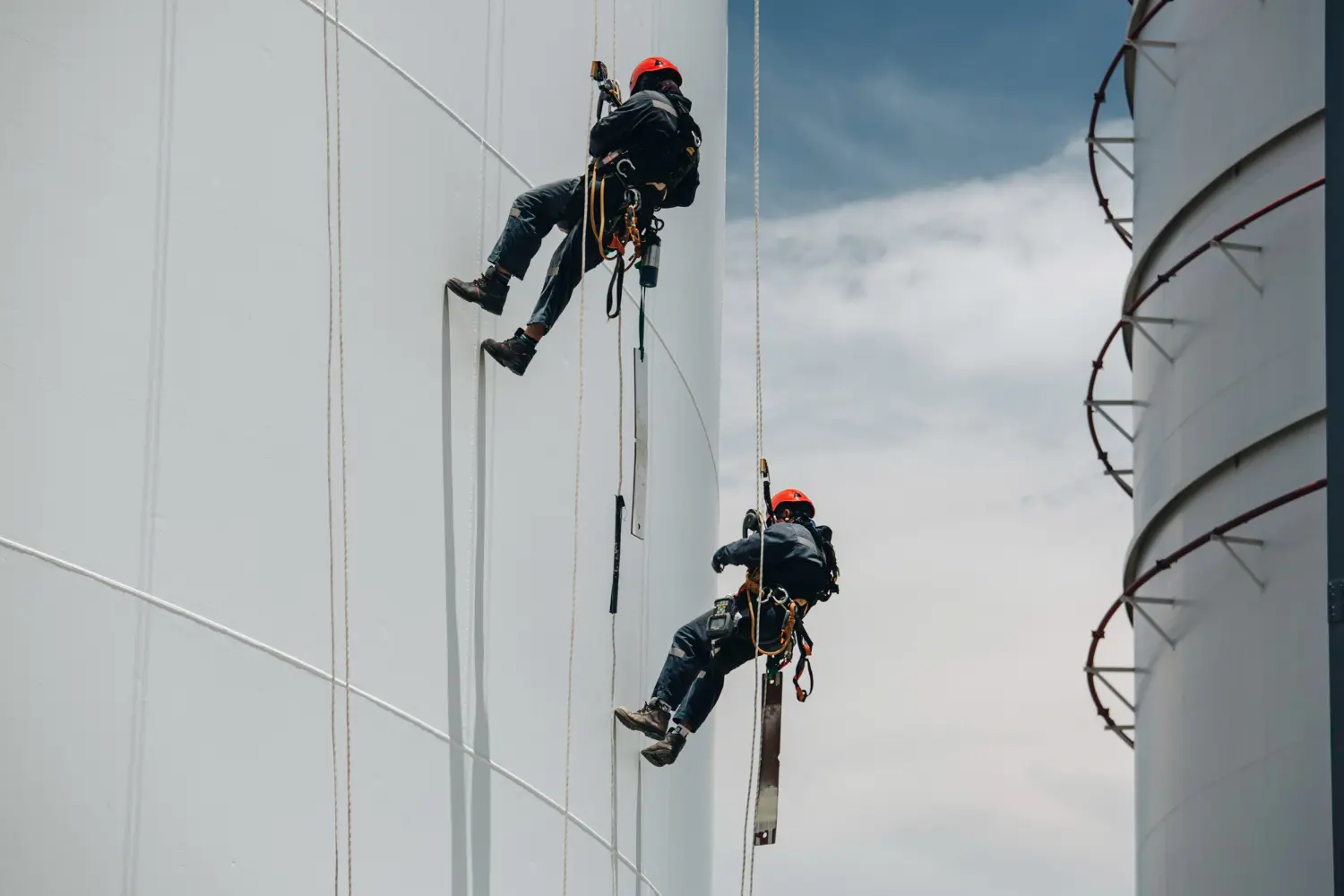 Equipe executa manutenção em superfície cilíndrica utilizando técnicas de acesso por corda com redundância de sistemas. 