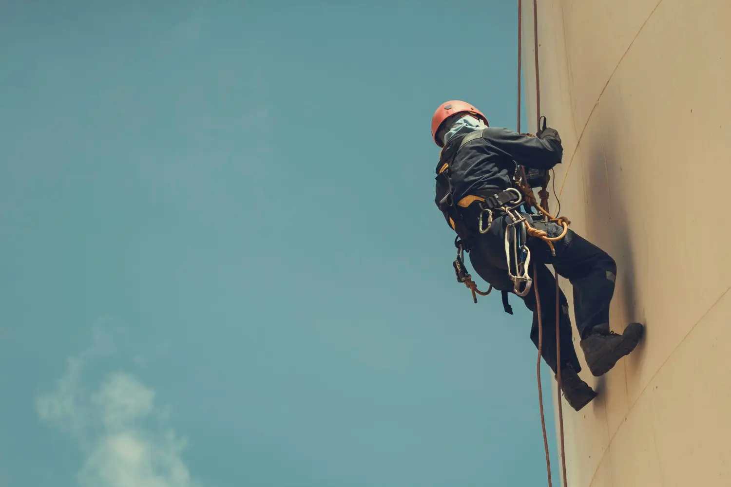Operador certificado realiza inspeção externa com sistema de acesso por corda, utilizando talabarte de posicionamento, trava-quedas guiado e capacete com jugular. 