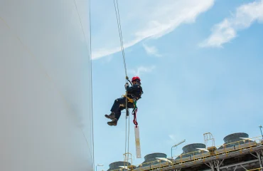 FOTO DESTAQUE Profissional executa atividade em altura utilizando técnicas de acesso por linha de vida, mantendo posicionamento seguro para inspeção e manutenção em superfície vertical de tanque industrial.