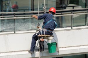 Execução de tarefa em fachada com cadeira suspensa: a segurança do operador depende da correta ancoragem, inspeção de equipamentos e aplicação das normas NR 18 e NR 35.