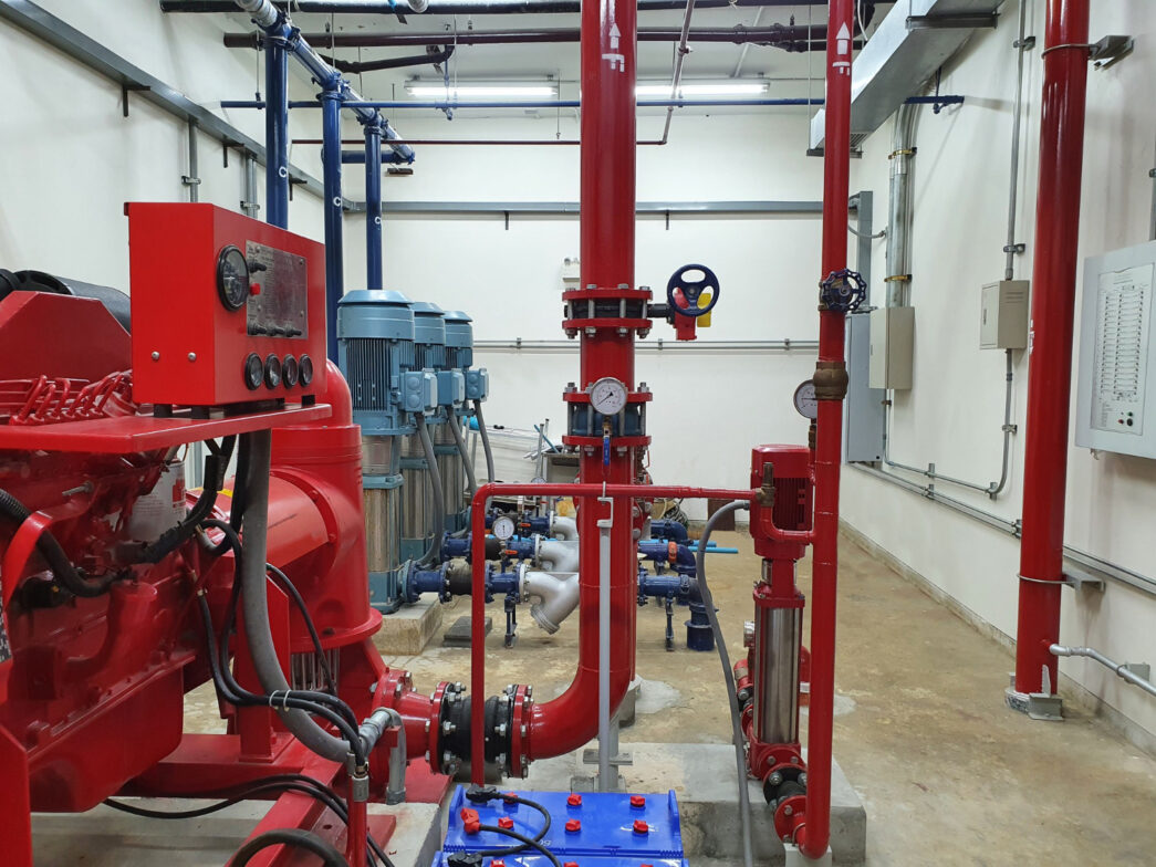 Sala de bombas do sistema de combate a incêndio – conformidade com a NFPA 20. Bomba principal (vermelha), bomba jockey (vertical menor) e painel de controle dedicados à pressurização da rede hidráulica contra incêndios.