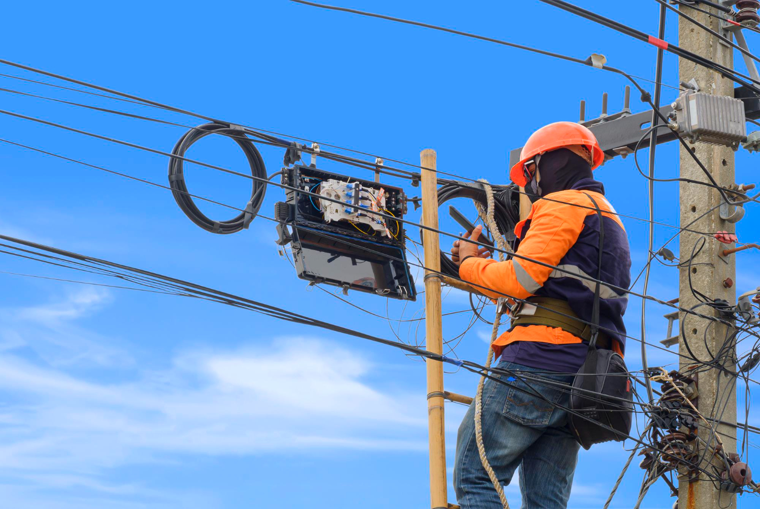 Intervenção técnica em rede de média/alta tensão com suporte em fibra óptica. O profissional utiliza EPI adequado e trabalha com isolamento tático em poste energizado, respeitando as diretrizes da NR 10 e NBR 16384.