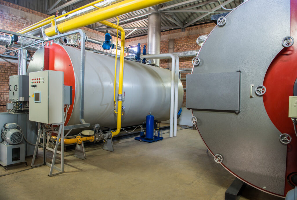 Ambiente industrial com dois grandes vasos de pressão horizontais tipo caldeira, integrados a um sistema de tubulações e válvulas de segurança - Curso Vaso de Pressão NFPA 85 e CGA G-2.1