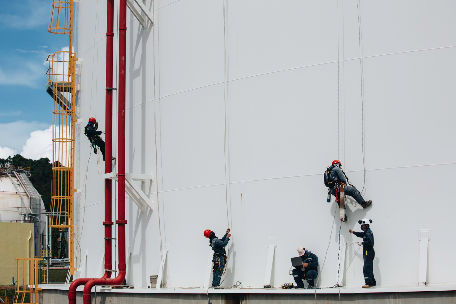 uma equipe técnica realizando trabalhos em altura por acesso por corda na estrutura externa de um tanque industrial de grande porte - Curso Acesso por Corda 2 NBR 15475