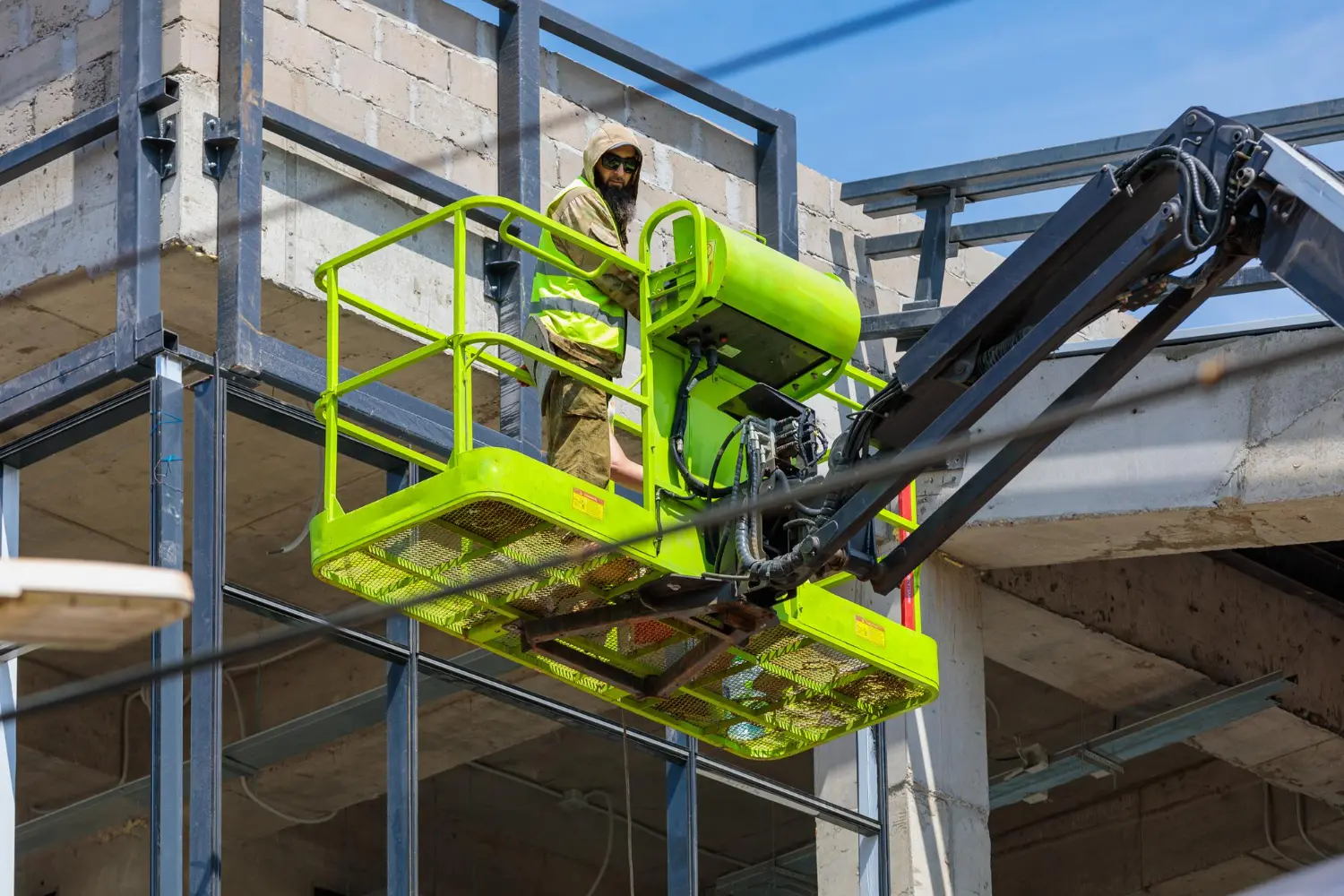 Plataforma elevatória pantográfica em uso, permite acesso seguro a estruturas verticais, devendo operar apenas com operador capacitado e EPI completo.