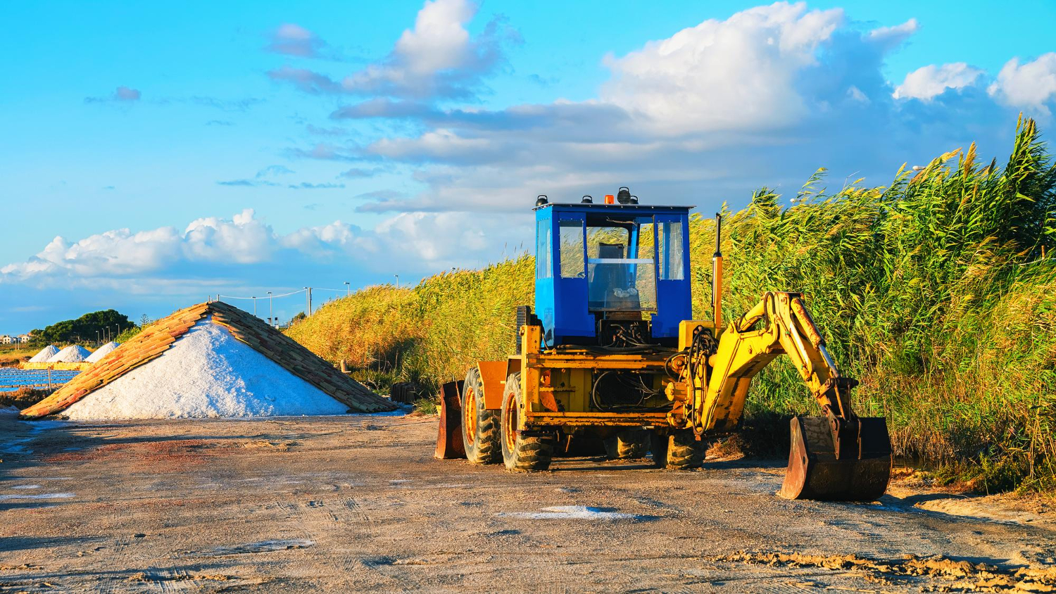 Retroescavadeira em ação na colheita de sal – Uma retroescavadeira robusta trabalhando na extração de sal, mostrando sua versatilidade na movimentação de materiais pesados em ambientes agrícolas e industriais. - Curso NR 12 Anexo 02 e 11.