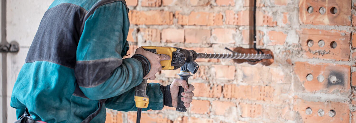 Técnico utilizando uma furadeira de impacto com broca SDS para perfuração de uma parede de tijolos, ferramenta essencial para trabalhos em alvenaria e concreto. - Curso Furadeira e Rosqueadeira.