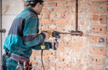 Técnico utilizando uma furadeira de impacto com broca SDS para perfuração de uma parede de tijolos, ferramenta essencial para trabalhos em alvenaria e concreto. Técnico utilizando uma furadeira de impacto com broca SDS para perfuração de uma parede de tijolos, ferramenta essencial para trabalhos em alvenaria e concreto. - Curso Furadeira e Rosqueadeira.