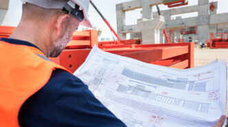 Engenheiro civil analisando o detalhamento executivo de uma estrutura de concreto armado, revisando seções de armaduras, especificações de fôrmas, e cotas do projeto no canteiro de obras. Essa etapa é crucial para verificar a compatibilidade entre o projeto estrutural e as condições reais de execução.
