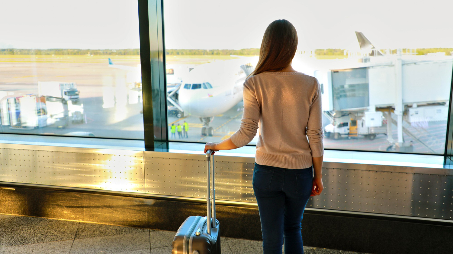Área interna do terminal aeroportuário com visão para o pátio, destacando uma aeronave conectada a uma manga de embarque telescópica. Esse equipamento é uma infraestrutura essencial para aeroportos modernos, integrando o terminal diretamente às aeronaves e melhorando a eficiência operacional. - Curso Operador Mangas Embarque.