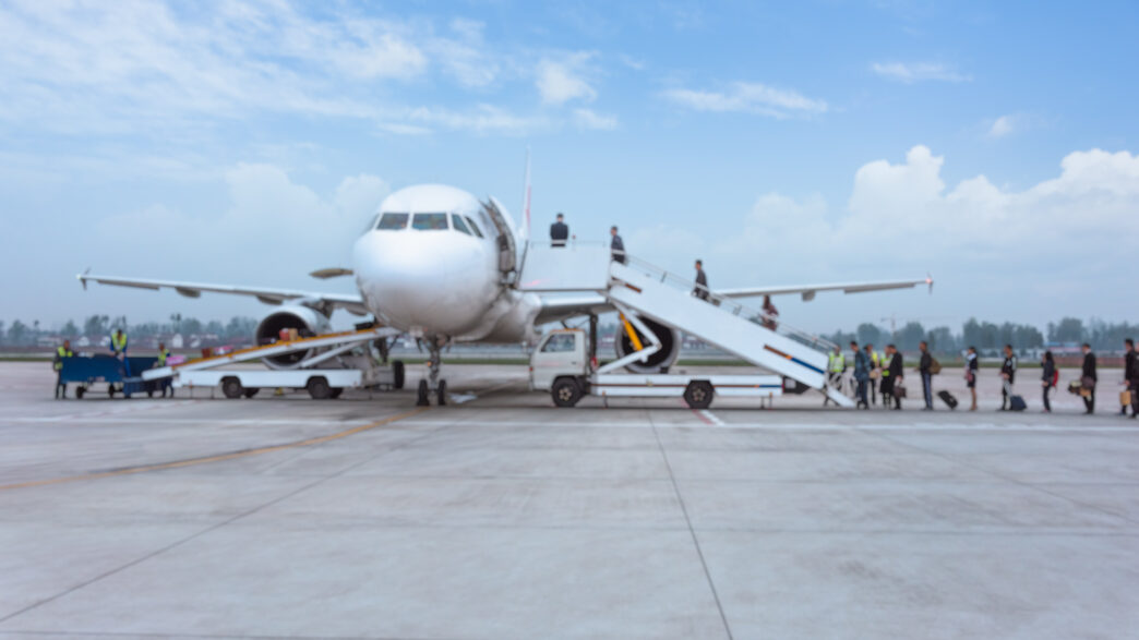 Processo de embarque realizado no pátio do aeroporto com o uso de escadas móveis, um método tradicional utilizado em operações onde mangas de embarque telescópicas não estão disponíveis ou viáveis, exigindo deslocamento externo dos passageiros entre o terminal e a aeronave. - Curso Operador Mangas Embarque.