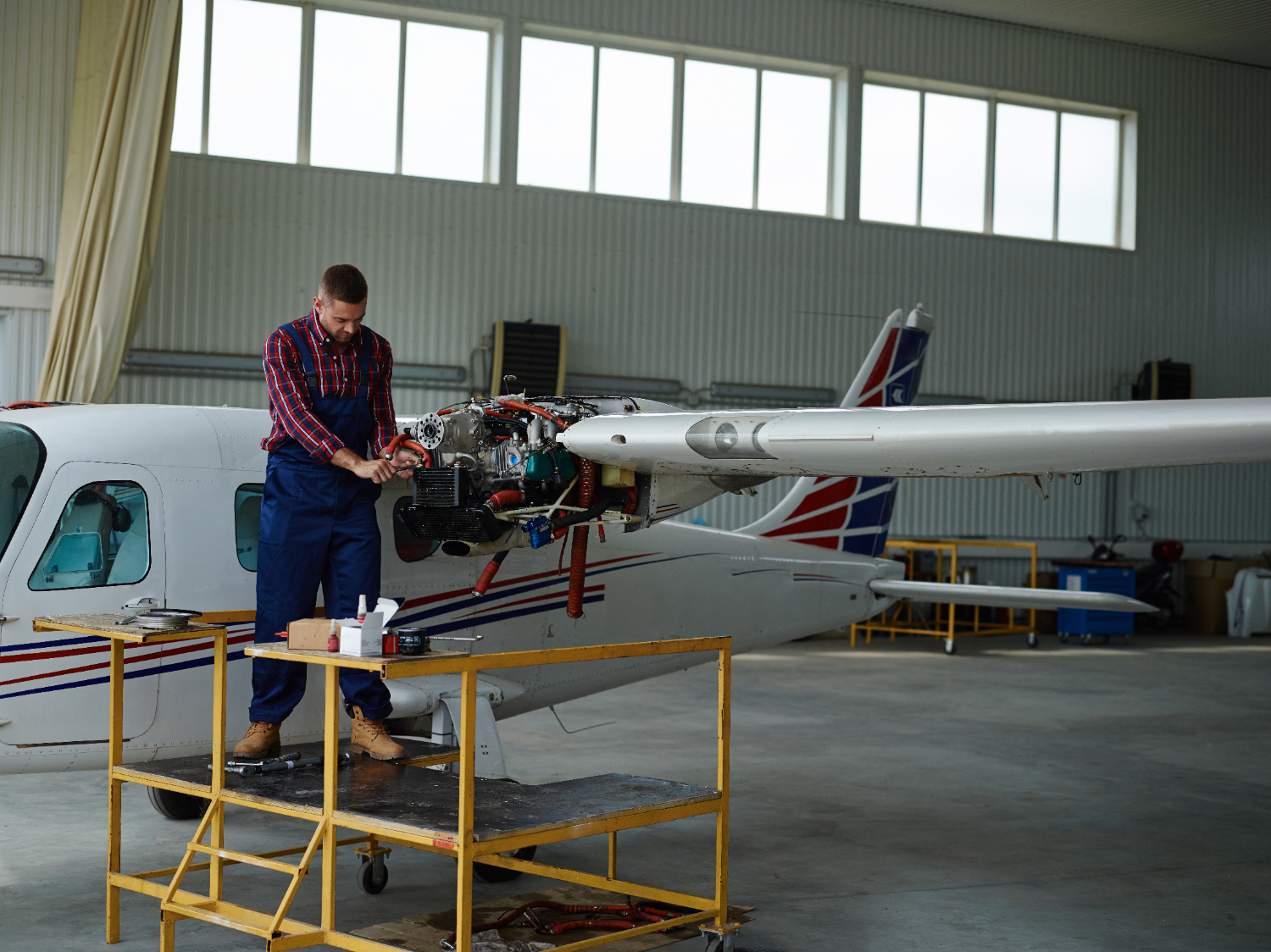 Mecânico realiza manutenção no motor de uma aeronave em um hangar, avaliando componentes e realizando ajustes para garantir a segurança operacional. - Curso Inspeção Aeronaves.