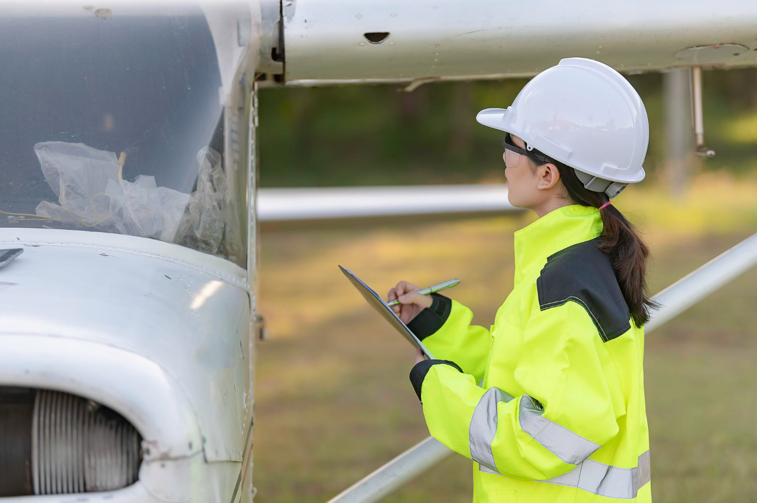 Técnica inspeciona as condições externas de uma aeronave leve, verificando o estado das superfícies e registrando observações em uma prancheta. - Curso Inspeção Aeronaves.