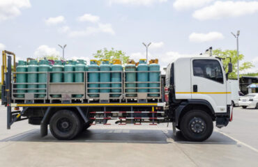 Caminhão leve com carroceria adaptada para o transporte de cilindros verticais de GLP (Gás Liquefeito de Petróleo). Os cilindros são protegidos por grades metálicas e organizados em fileiras, conforme regulamentações de segurança para transporte de gases inflamáveis em áreas urbanas. O objetivo do Curso Transporte de Cilindros de Gases é capacitar os participantes a realizarem o transporte seguro, eficiente e conforme a legislação vigente, garantindo a integridade dos cilindros e minimizando os riscos associados ao manuseio e deslocamento. Além disso, busca conscientizar sobre os perigos potenciais, ensinar práticas adequadas de movimentação, fixação e armazenamento, bem como preparar os profissionais para identificar irregularidades e responder adequadamente a situações de emergência, promovendo a segurança de pessoas, equipamentos e do ambiente.