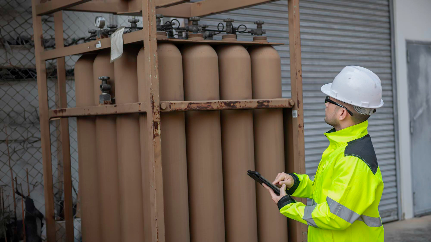 Técnico utilizando equipamento para checagem de cilindros de gases em contêiner. Equipamento de proteção e ambiente controlado conforme legislação de segurança no trabalho. - Curso Legislação Cilindro Gases.