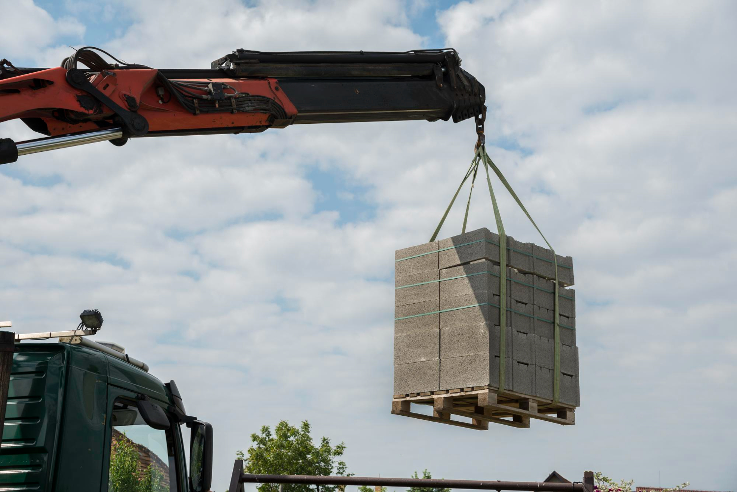 caminhão equipado com guindaste articulado realizando o içamento de um pallet contendo blocos de concreto