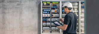 Técnico inspecionando um quadro de distribuição elétrica com auxílio de um tablet, assegurando a conformidade com o padrão de entrada de energia e a segurança na instalação. - Curso Padrão Entrada Energia.