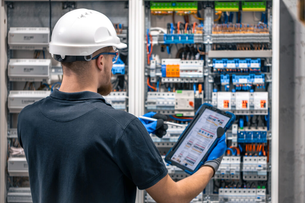 Eletricista com tablet ajustando circuito na caixa de junção - Curso Inspeção Instalações Elétricas IEC60079-17