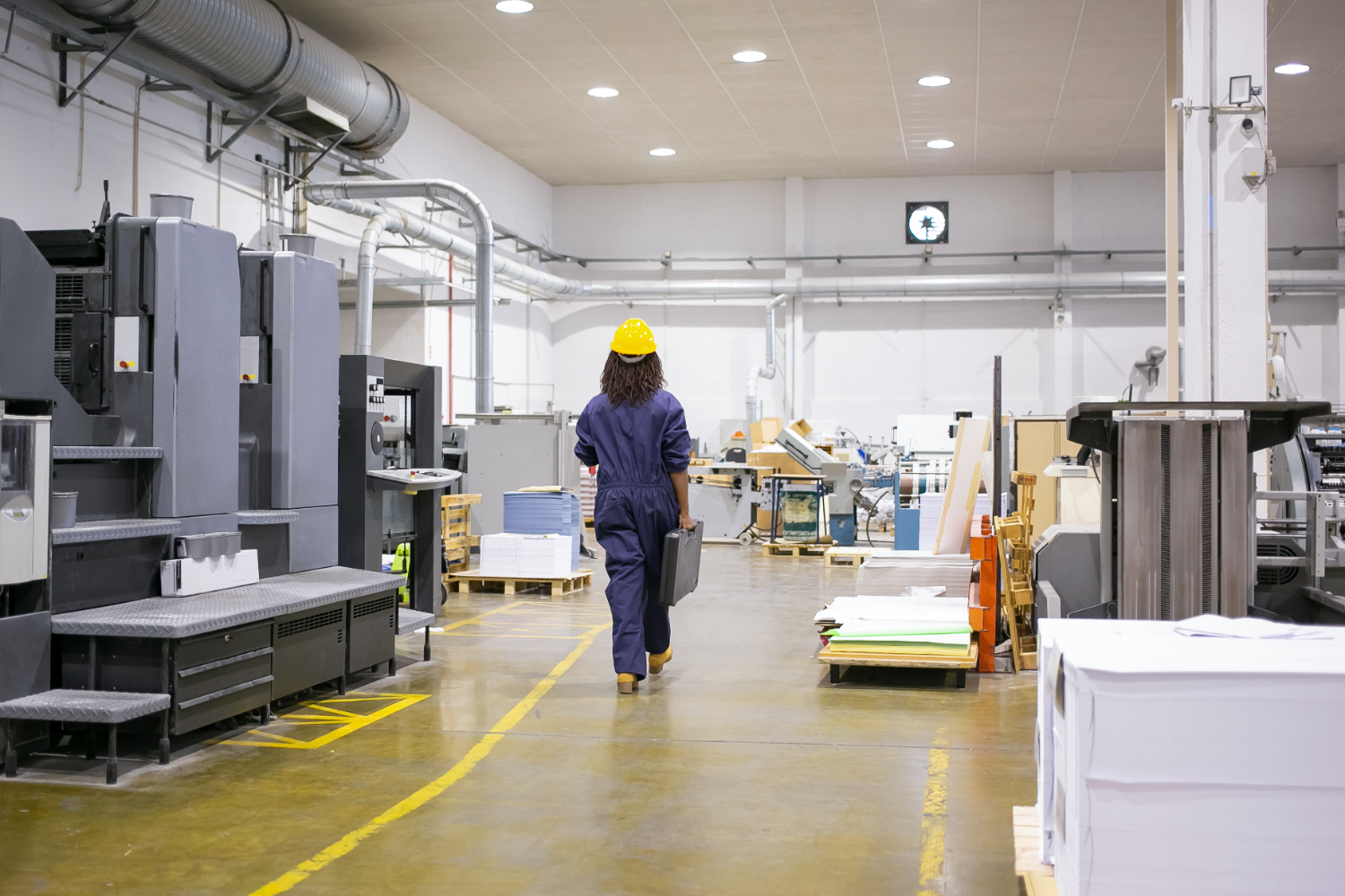 Técnica em manutenção industrial se desloca pela sala de máquinas equipada com sistemas de produção automatizados, pronta para inspeção ou intervenção técnica preventiva. - Curso Sala Máquinas Árabe.