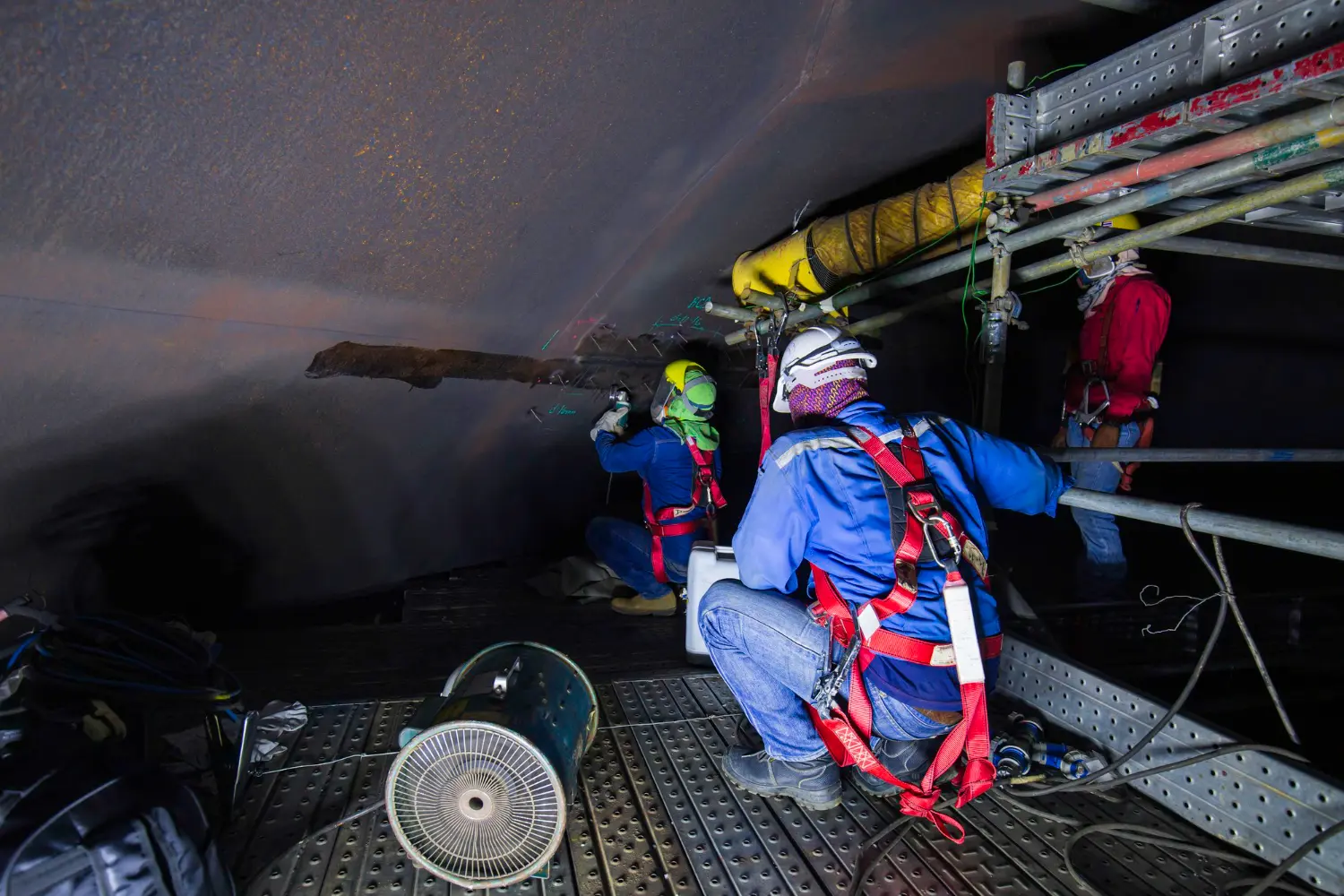 Equipe técnica realizando inspeção em espaço confinado com ventilação mecânica, análise de gases e uso integral de EPIs.