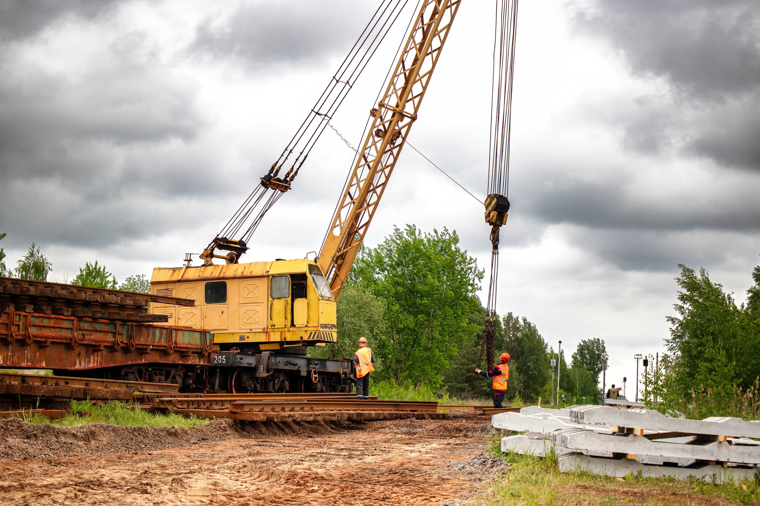 Operação técnica com guindaste ferroviário executando içamento de componentes estruturais de linha férrea. A atividade exige alinhamento entre operador, rigger e ambiente, reforçando a importância da sinalização, sincronia e percepção do terreno.