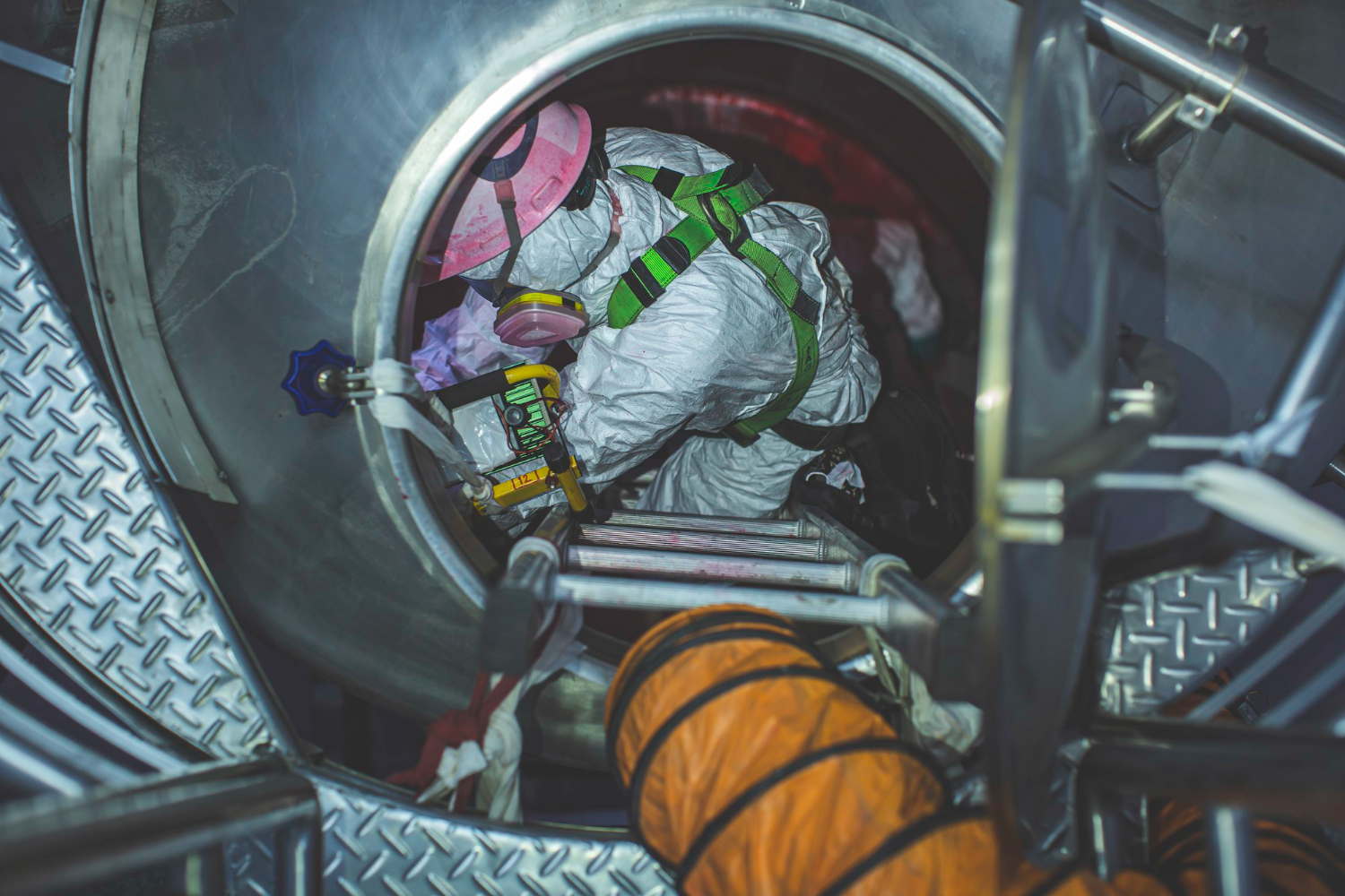 Authorized professional in confined space entry through a flange, using a lifeline, multi-gas detector, and forced ventilation.