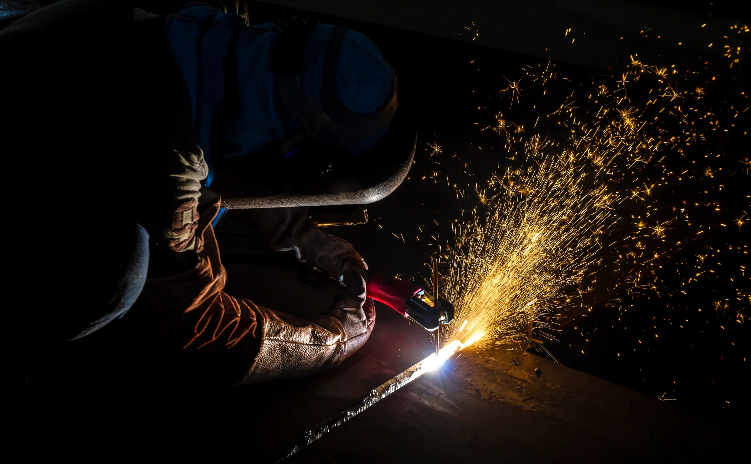 Operação com equipamento de soldagem em ambiente com pouca luz. A visibilidade do arco reforça a importância de barreiras de proteção e EPI com certificação NR 6.