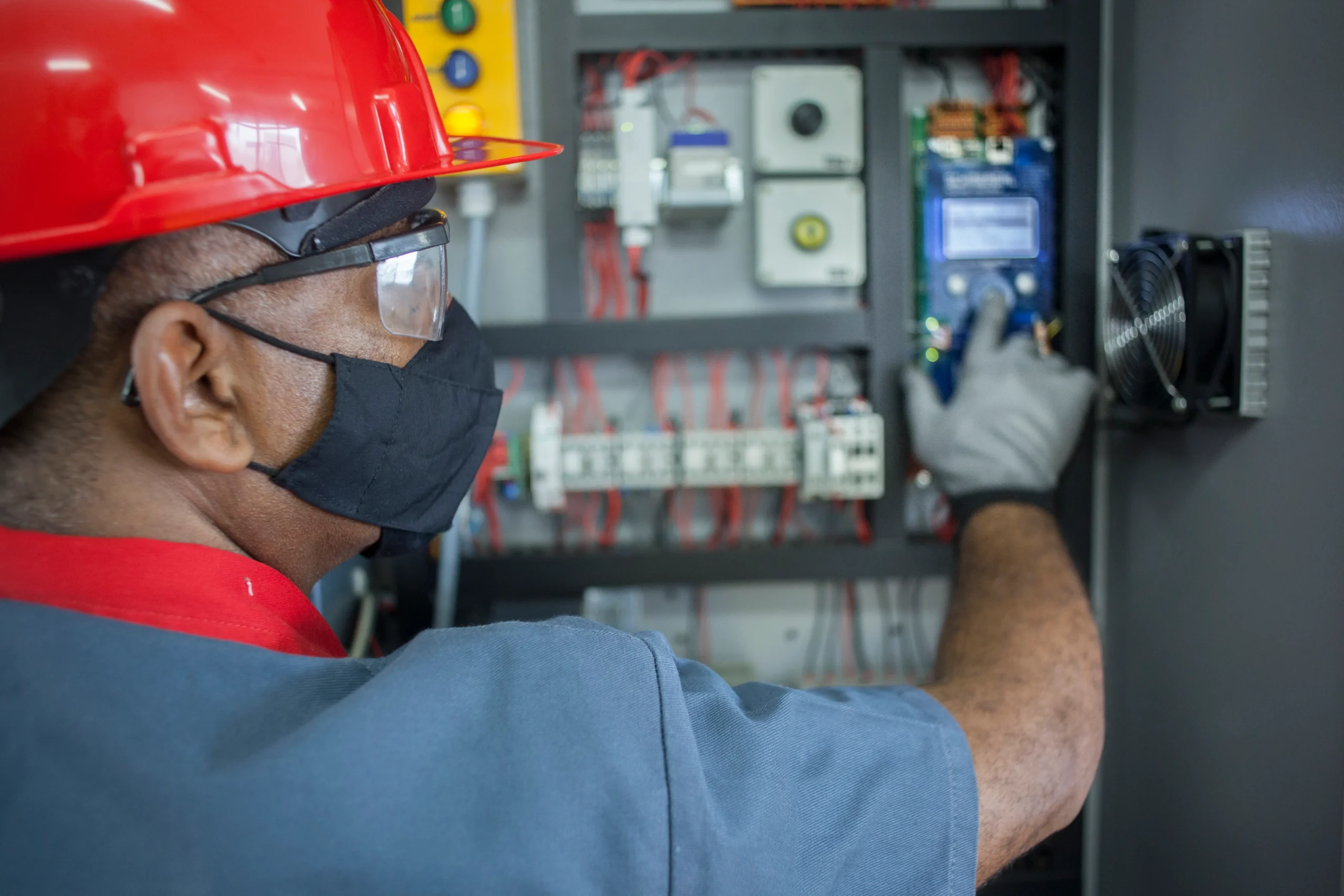 Trabalhador atuando em sistema de comando elétrico com EPI adequado e procedimento autorizado.