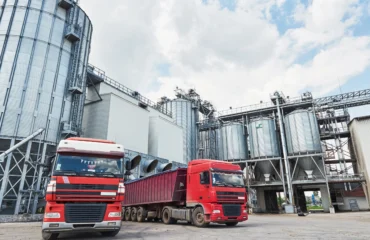 2 Imagem apresenta área logística com silos metálicos, passarelas e caminhões em operação, destacando a integração entre estrutura, transporte e carregamento.
