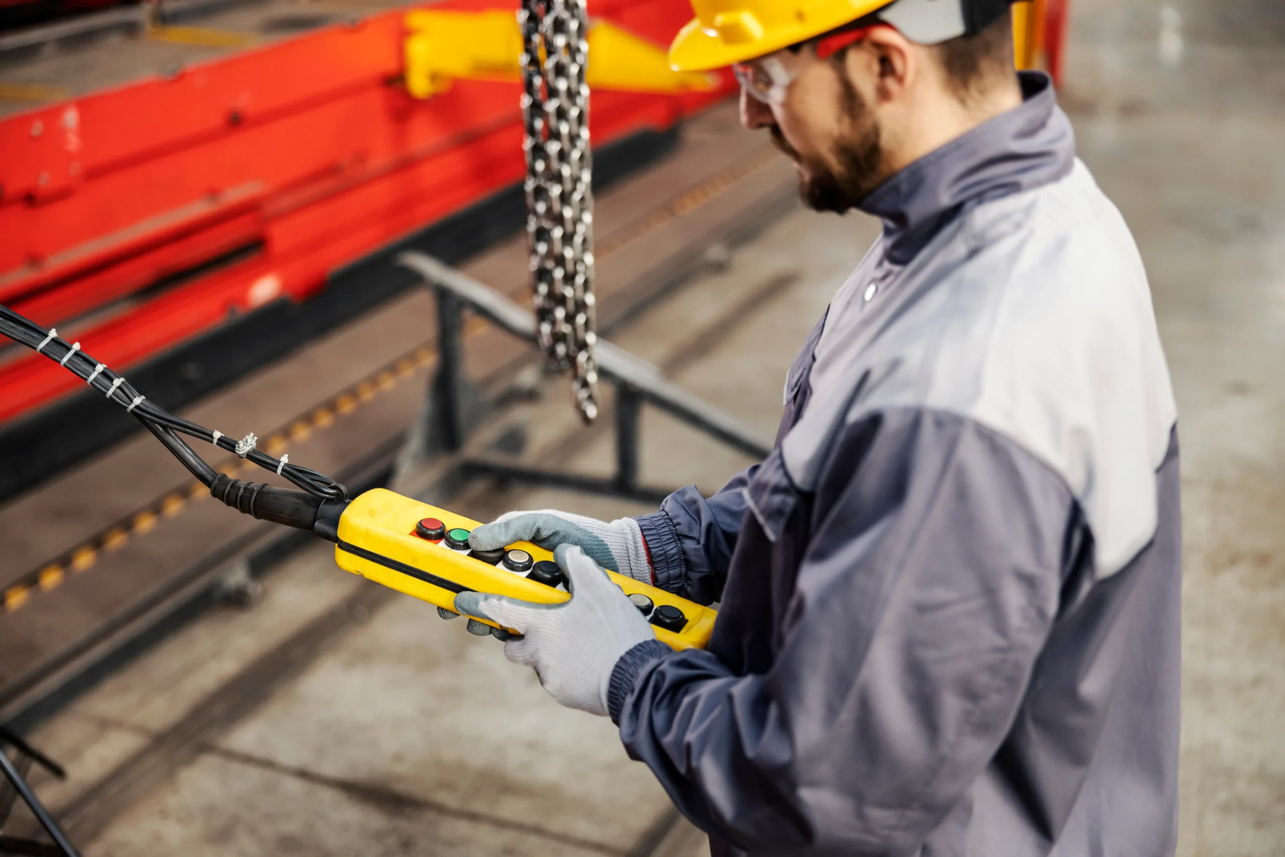 1 Profissional realiza inspeção funcional de talha elétrica por meio de comando pendente, verificando resposta dos controles, funcionamento dos botões de emergência e comportamento do sistema de elevação conforme critérios de segurança.