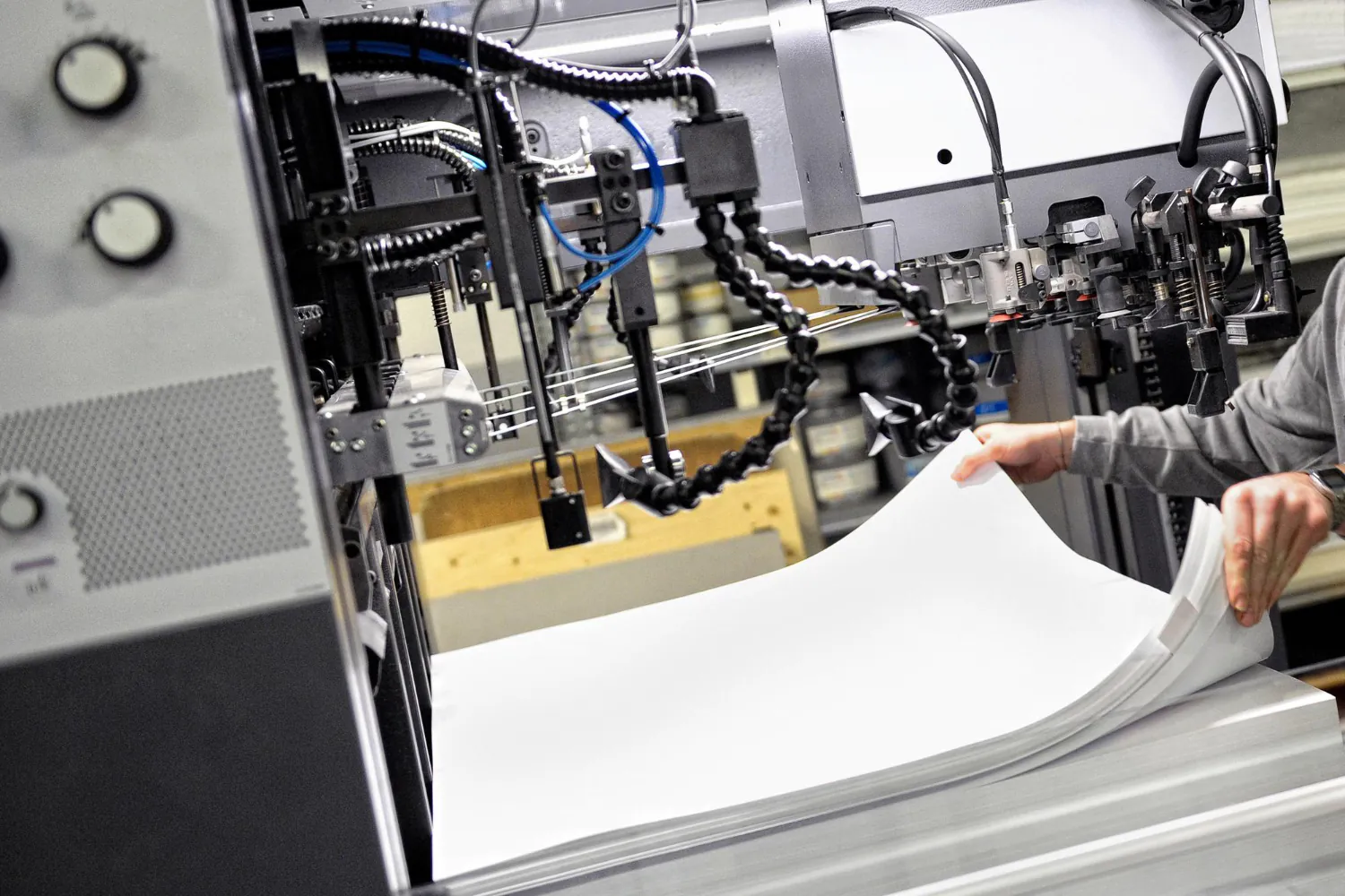 Detalhe do sistema de alimentação automática da cortadeira: sensores, ventosas e braços mecânicos otimizam o fluxo do papel e exigem proteção contra aprisionamento e esmagamento. - Curso Operador de Cortadeira de Papel.