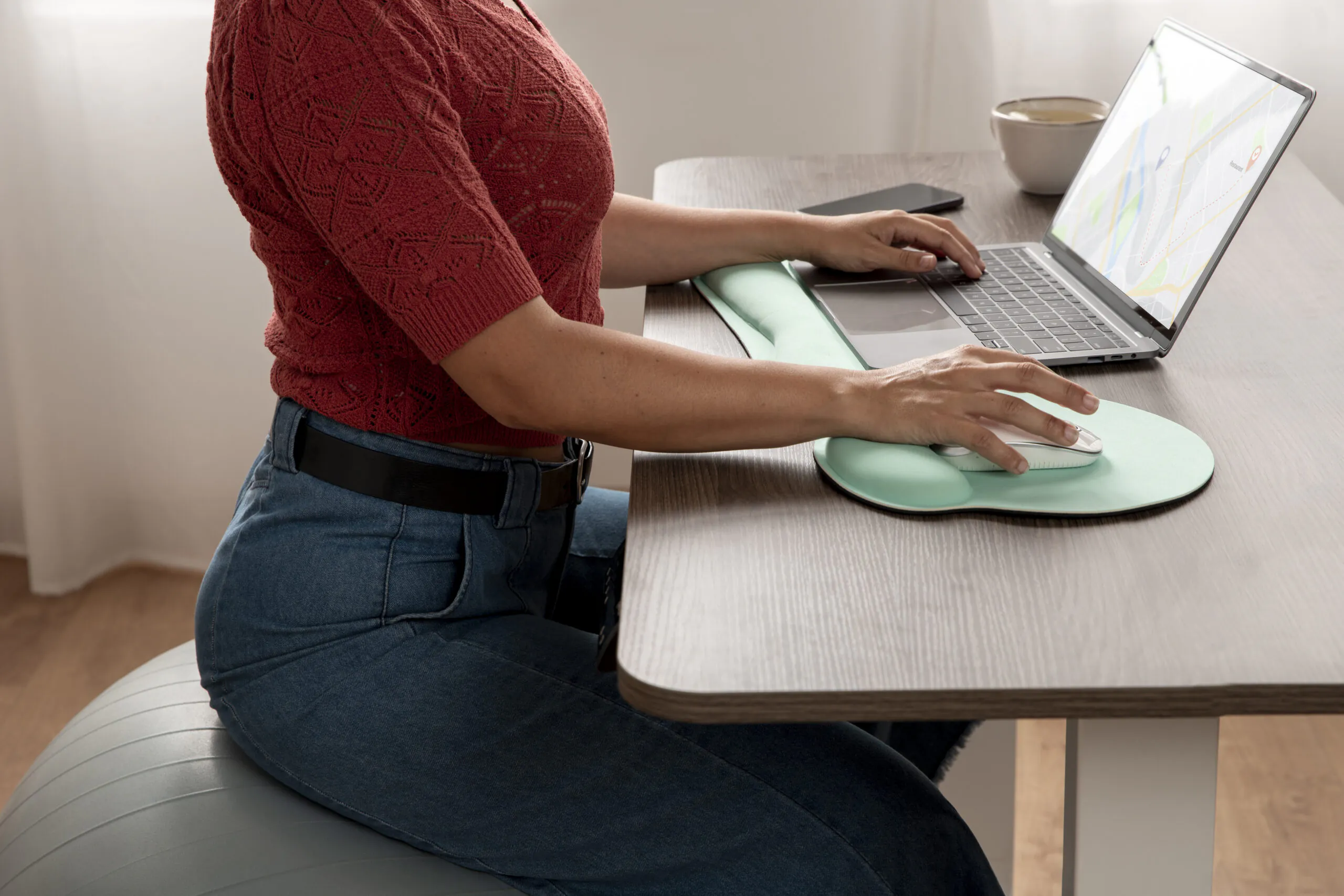 pessoa trabalhando em um notebook sobre uma mesa, utilizando apoio ergonômico - Curso Laudo Ergonômico