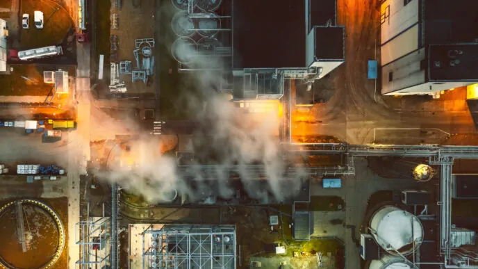 Vista aérea de uma instalação industrial fervilhante, com vapores escapando das tubulações e uma iluminação dramática, criando uma sensação de instabilidade em um ambiente potencialmente explosivo.