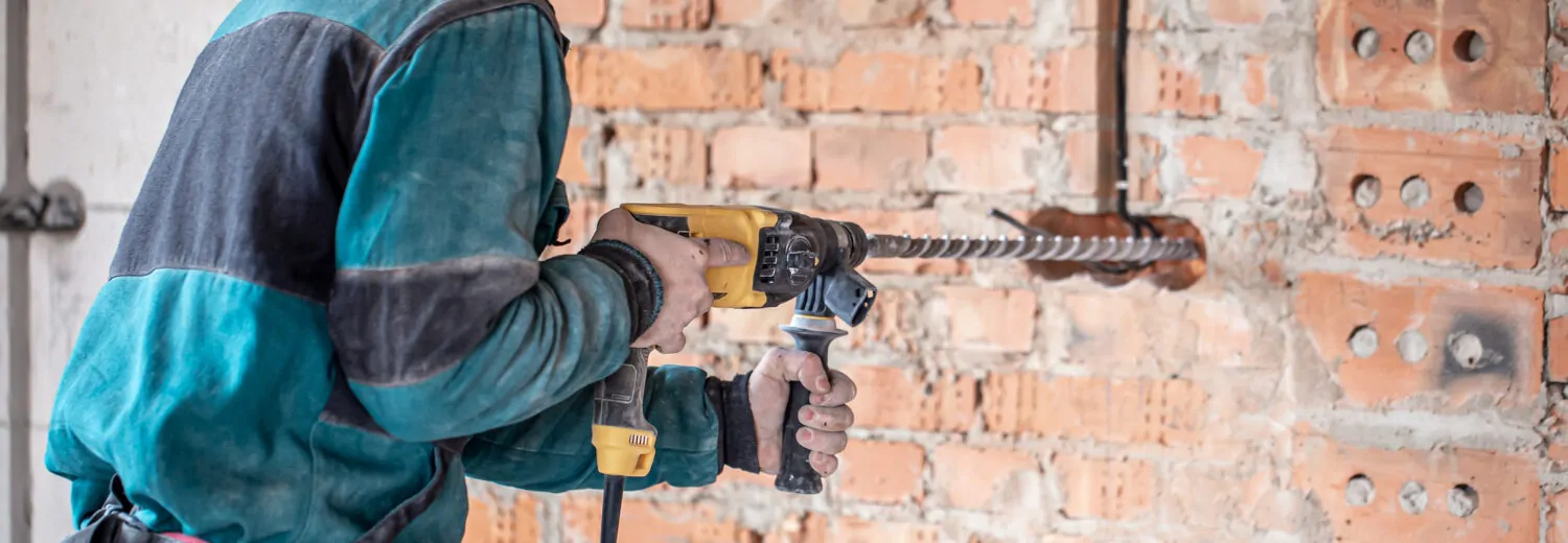 Técnico utilizando uma furadeira de impacto com broca SDS para perfuração de uma parede de tijolos, ferramenta essencial para trabalhos em alvenaria e concreto. - Curso Furadeira e Rosqueadeira.