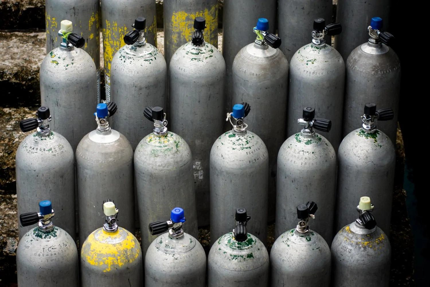  Conjunto de cilindros de gases industriais organizados para armazenamento, evidenciando a necessidade de inspeções regulares para evitar vazamentos ou danos. - Curso Cilindros Gases Industriais.